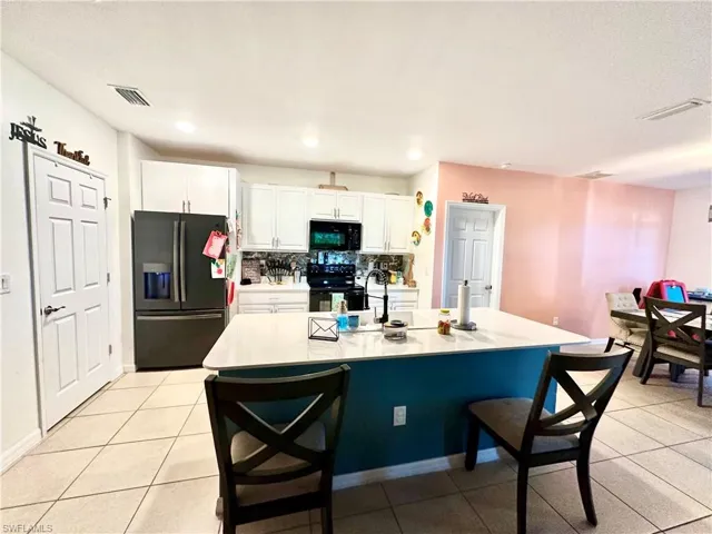 Kitchen with white cabinetry, light countertops, a breakfast bar, decorative backsplash, and black appliances