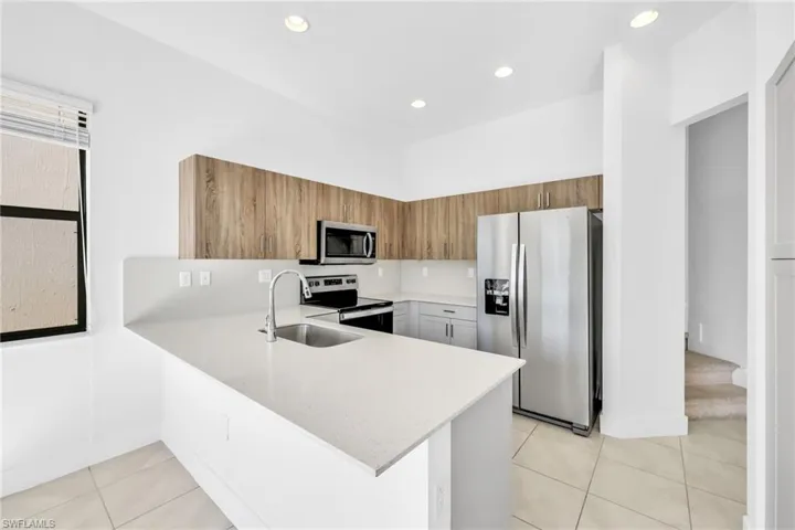 Kitchen featuring brown cabinets, stainless steel appliances, a peninsula, recessed lighting, and light granite countertops