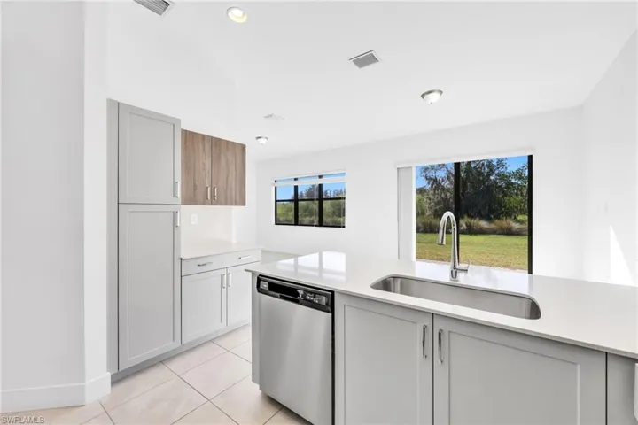 Kitchen with stainless steel dishwasher, light stone counters, and light tile patterned flooring