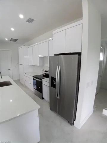 Kitchen with white cabinetry, sink, light stone countertops, and stainless steel appliances