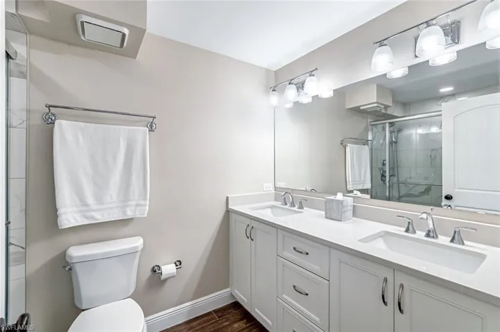 Full bath with double vanity, a stall shower, and wood finished floors