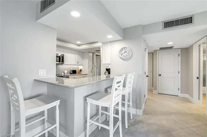 Kitchen featuring stainless steel microwave, recessed lighting, white cabinets, a breakfast bar area, and tasteful backsplash