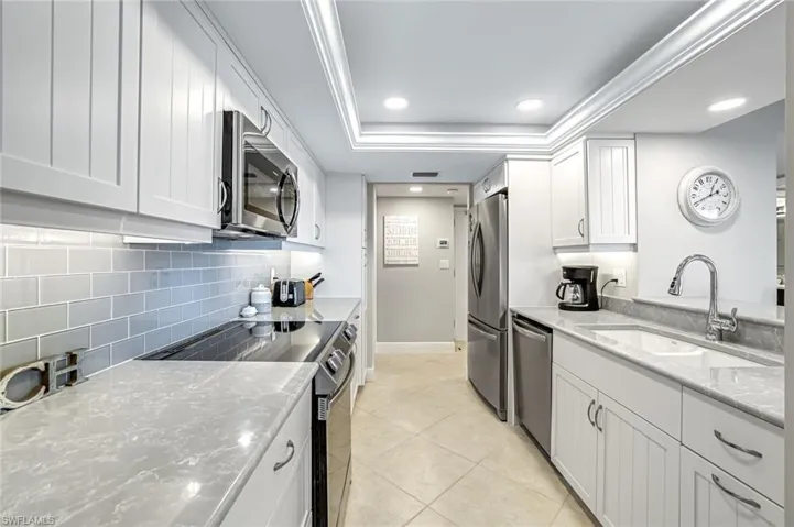 Kitchen featuring appliances with stainless steel finishes, decorative backsplash, a tray ceiling, white cabinets, and light stone countertops