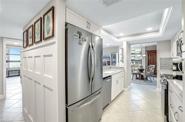 Kitchen with appliances with stainless steel finishes, light tile patterned floors, white cabinets, a raised ceiling, and recessed lighting