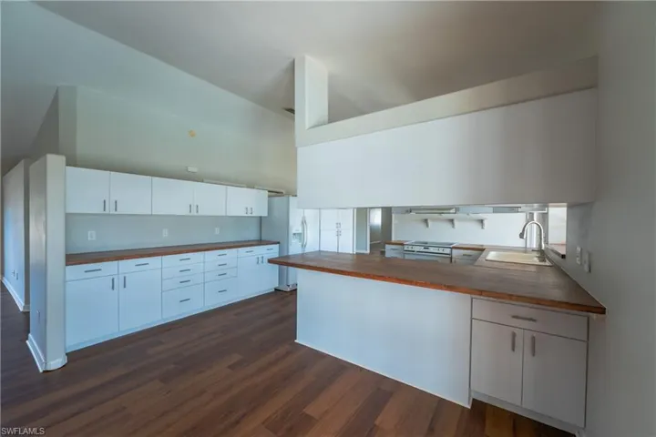 Kitchen with white cabinets, dark wood-style floors, white appliances, and butcher block counters