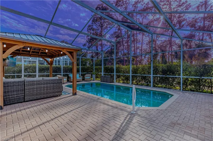 Pool at dusk under screened in lanai, with covered gazebo area