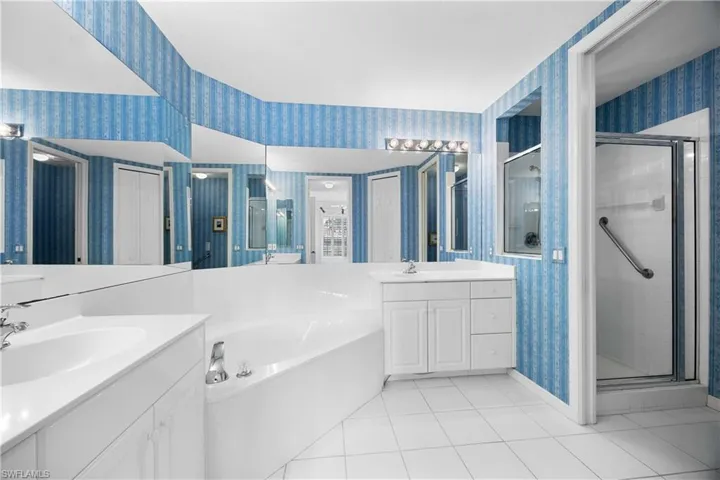 Full bathroom with wallpapered walls, light tile patterned floors, a stall shower, a bath, and two vanities
