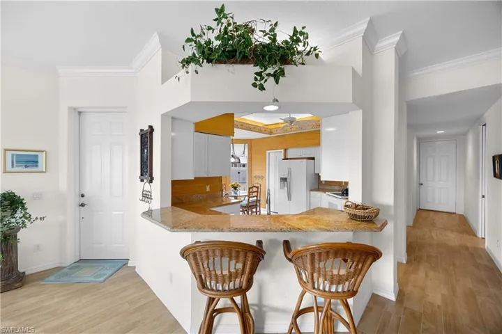 Kitchen featuring light wood finished floors, ornamental molding, white refrigerator with ice dispenser, white cabinetry, and a kitchen breakfast bar