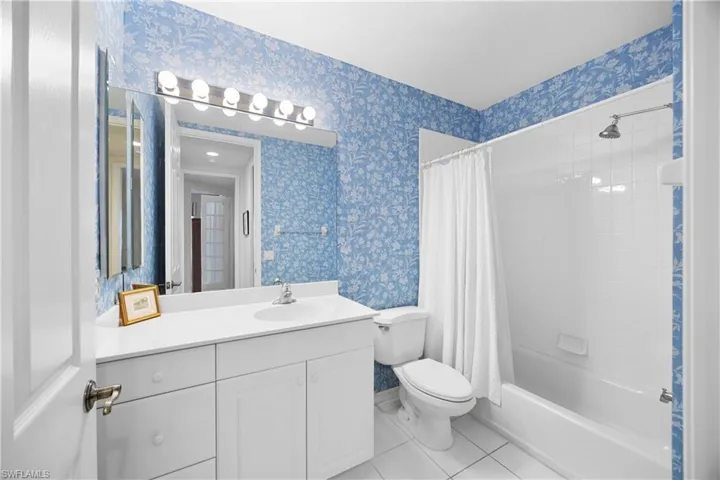 Full bath featuring light tile patterned flooring, vanity, shower / tub combo, and wallpapered walls