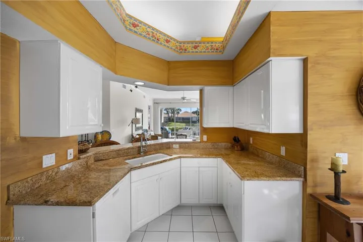 Kitchen with dark stone counters, light tile patterned floors, white cabinetry, wood walls, and a ceiling fan