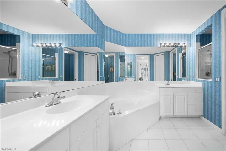 Full bath with wallpapered walls, a shower stall, light tile patterned floors, a bath, and two vanities