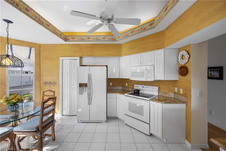 Kitchen with white appliances, white cabinets, a tray ceiling, light tile patterned floors, and hanging light fixtures