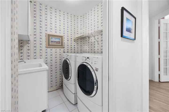 Laundry room featuring washer and clothes dryer, cabinet space, wallpapered walls, and light tile patterned flooring