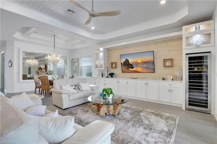 Living room with wood ceiling, light tile patterned floors, a raised ceiling, beverage cooler, and ceiling fan with notable chandelier