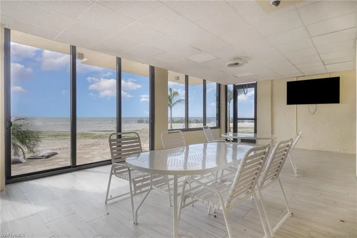 Sunroom / solarium featuring expansive windows, wood finish floors, a textured wall, view of water and beach, and a drop ceiling