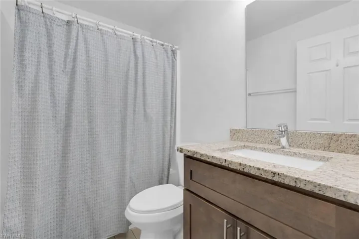 Granite-style countertop with an integrated sink, wood-finish vanity, and a wall-mounted mirror