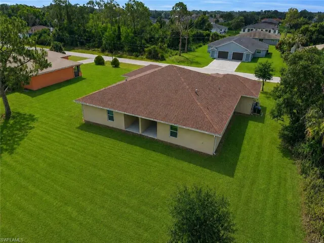 Expansive green lawn surrounds a single-story structure with a brown shingle roof, light-colored exterior, and an integrated covered patio area