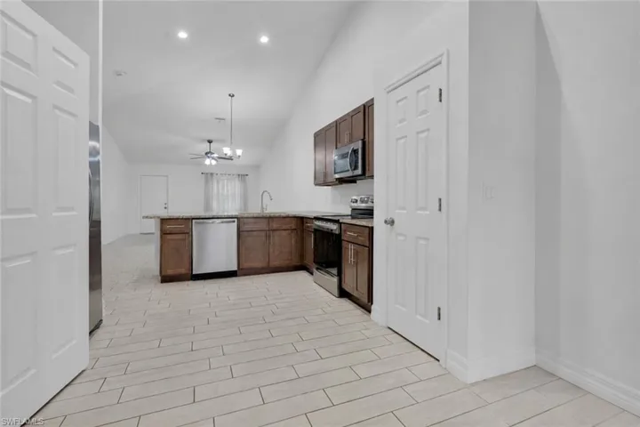 Kitchen featuring wood-finish cabinetry, stainless steel appliances, and a peninsula with a stone-finish countertop