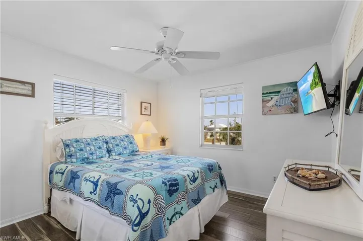 Bedroom featuring dark hardwood / wood-style flooring, multiple windows, ornamental molding, and ceiling fan