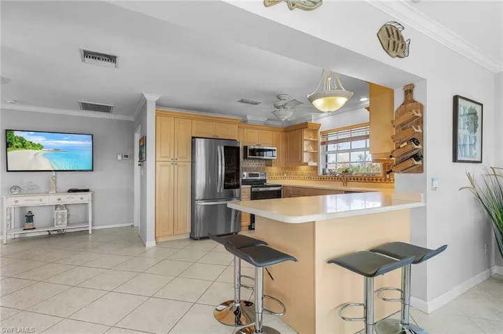 Kitchen with kitchen peninsula, stainless steel appliances, ornamental molding, a breakfast bar, and light brown cabinets