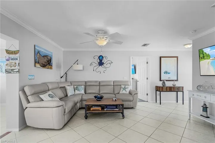 Living room featuring ornamental molding, light tile patterned floors, and ceiling fan