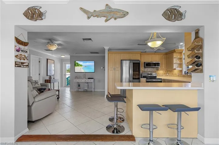 Kitchen featuring kitchen peninsula, decorative backsplash, appliances with stainless steel finishes, a breakfast bar, and crown molding