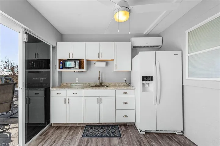 Kitchen with a wall unit AC, white cabinets, dark hardwood / wood-style flooring, white fridge with ice dispenser, and sink