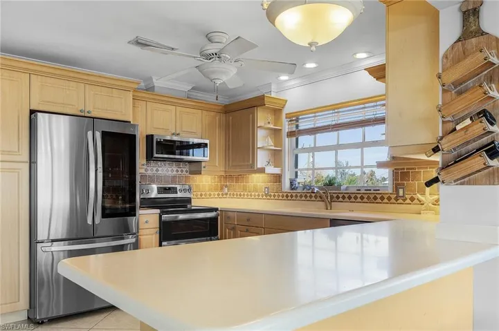 Kitchen with appliances with stainless steel finishes, kitchen peninsula, tasteful backsplash, and light tile patterned floors