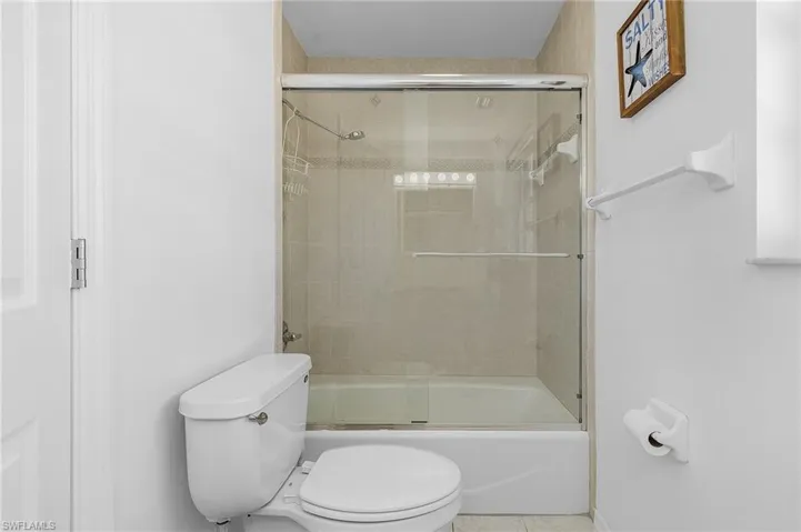 Bathroom with bath / shower combo with glass door and toilet