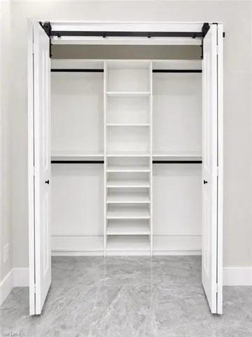 Bifold barn doors open to a custom closet system featuring a central shelving unit, double hanging rods, and light gray tile flooring