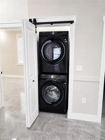 Laundry closet featuring a stacked washer and dryer, barn door hardware, and modern tile flooring