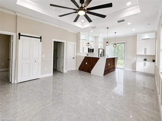 Contemporary kitchen and open living area featuring large format porcelain tile flooring, a tray ceiling with a black ceiling fan, white shaker cabinetry with undermount lighting, a two-tone kitchen island with pendant lighting, and a sliding glass door
