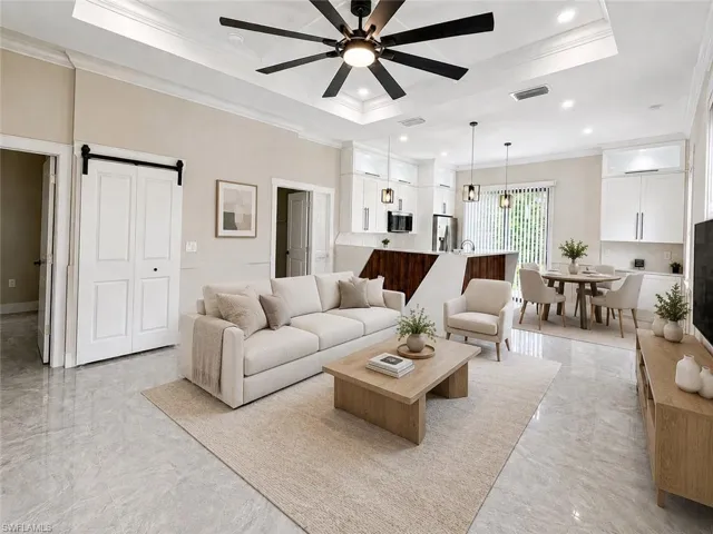 Open-concept living area featuring light gray tile flooring, a tray ceiling with a dark-bladed ceiling fan, and crown molding
