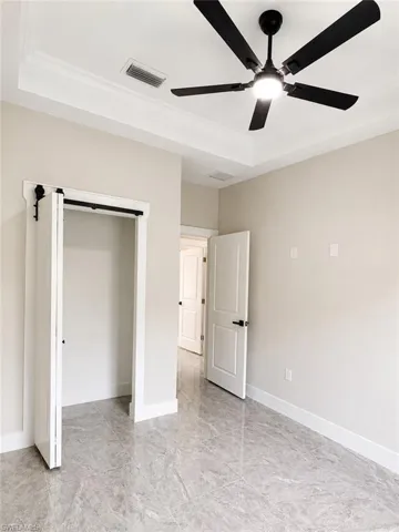 Recessed tray ceiling with crown molding, modern black ceiling fan, large format tile flooring, white baseboards, and a barn door entry