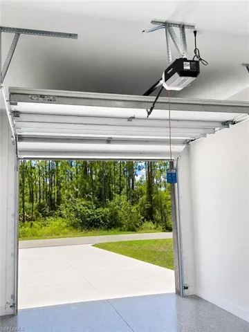 Attached garage with an automatic opener, featuring a durable epoxy floor coating, concrete driveway, and a natural tree-lined backdrop