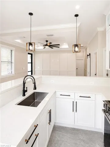 Modern kitchen featuring white cabinetry, light-toned countertops, a stainless steel sink with a matte black faucet, and pendant lighting