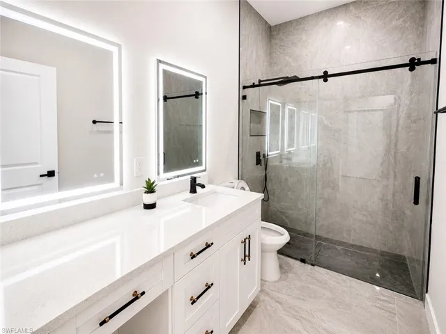 Bathroom featuring a quartz countertop vanity with double illuminated mirrors, a glass-enclosed walk-in shower with a sliding barn door, and large format tile flooring