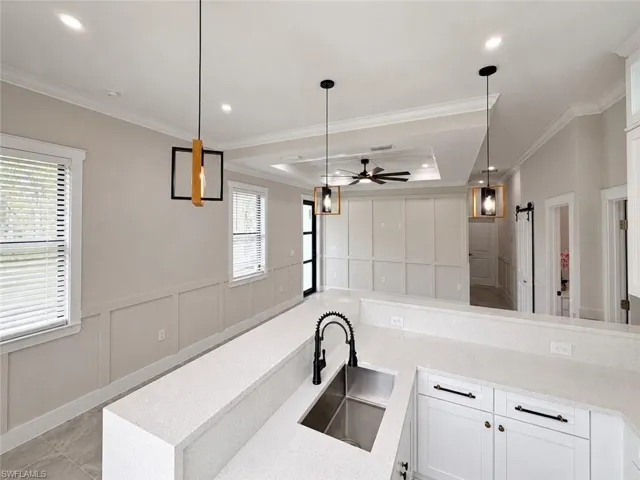 Open-concept kitchen featuring an undermount stainless steel sink, black gooseneck faucet, light-toned countertops, white cabinetry, and pendant lighting