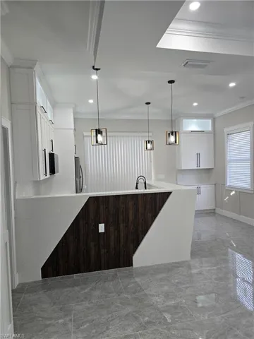 Modern kitchen featuring white cabinetry, a large kitchen island with wood-finish paneling, gray tile flooring, recessed lighting, and contemporary pendant fixtures