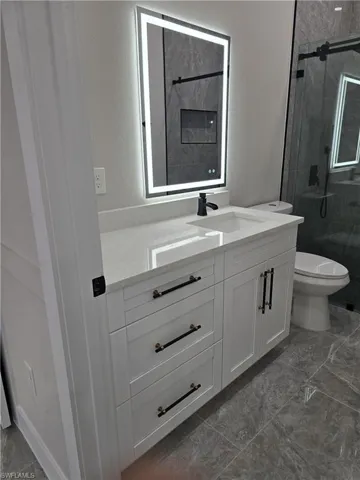 Modern bathroom vanity featuring a lighted mirror, integrated sink, and matte black fixtures