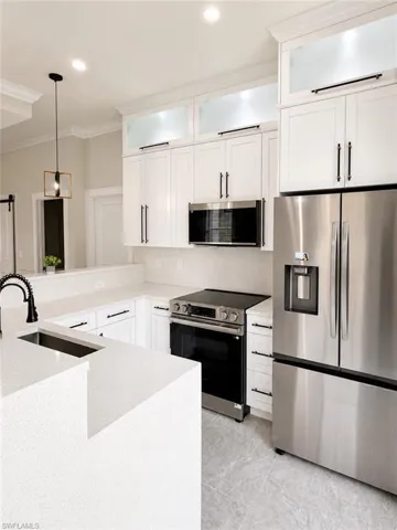 Contemporary kitchen featuring white cabinetry with matte black hardware, integrated stainless steel appliances, light-toned countertops, and a coordinating island with an undermount sink