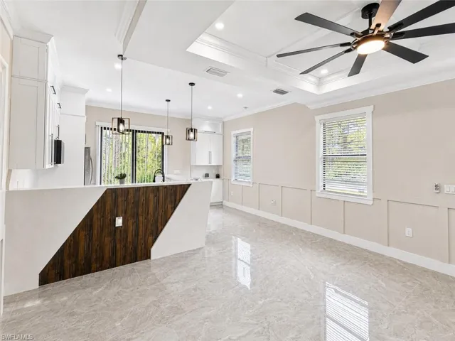 Spacious open-concept interior featuring light gray porcelain tile flooring, a kitchen island with a wood-finish accent panel, and white cabinetry