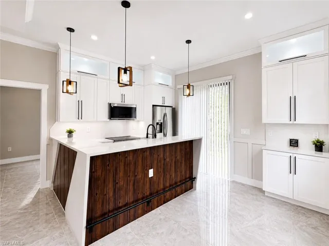 Modern kitchen featuring an extended island with a wood-finish base and light-toned countertop, complemented by white cabinetry with dark hardware