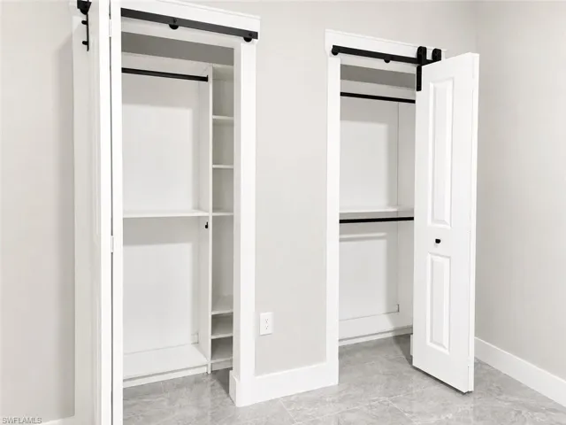Dual bi-fold closets featuring custom shelving and hanging rods, set against light gray walls with white baseboards and trim, and gray tile flooring