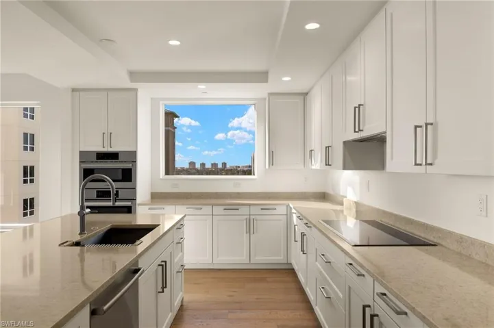 Lots of cabinets in this light and airy Kitchen featuring light stone counters, white cabinetry, light wood-style floors, stainless steel appliances, and a raised ceiling