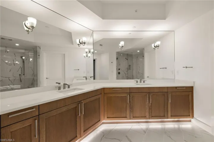 Master bathroom with double vanity, a marble finish shower, light marble finish flooring