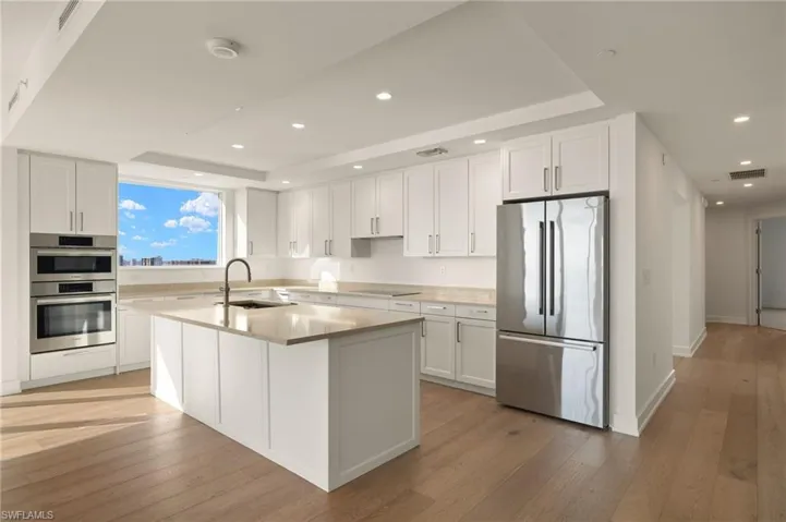 Spacious kitchen featuring appliances with stainless steel finishes, white cabinetry, recessed lighting, a tray ceiling, and light wood-style floors