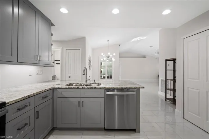 Kitchen with gray cabinets, lofted ceiling, sink, stainless steel dishwasher, and kitchen peninsula