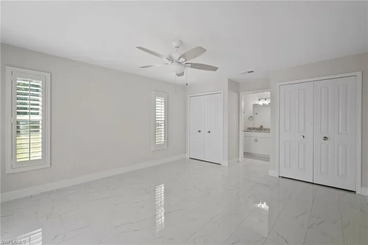Unfurnished bedroom with ceiling fan, ensuite bath, and two closets