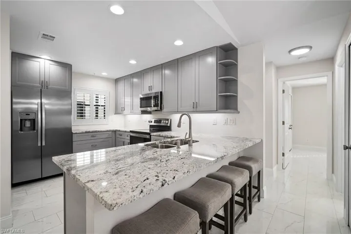 Kitchen with a breakfast bar, sink, gray cabinets, kitchen peninsula, and stainless steel appliances